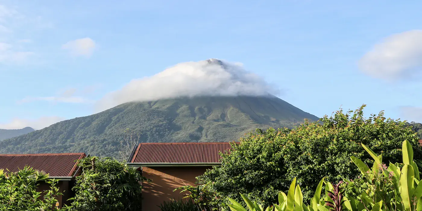 Arenal volcano rising in a near-perfect cone above dense green rainforest, its summit partly veiled in cloud