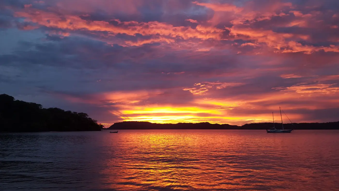 Orange and purple sunset over Bahía Culebra in the Gulf of Papagayo, with a sailboat at anchor
