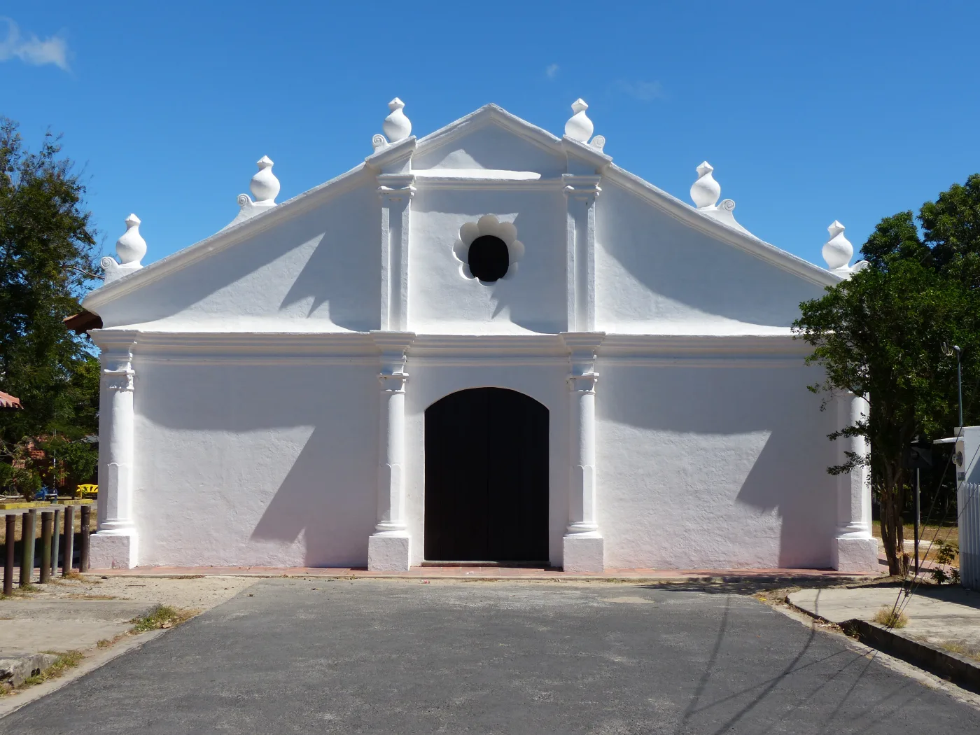 The whitewashed adobe facade of the Ermita de Nuestro Señor de la Agonía in Liberia, Costa Rica, its gabled roofline topped with six pinnacles above an arched wooden door