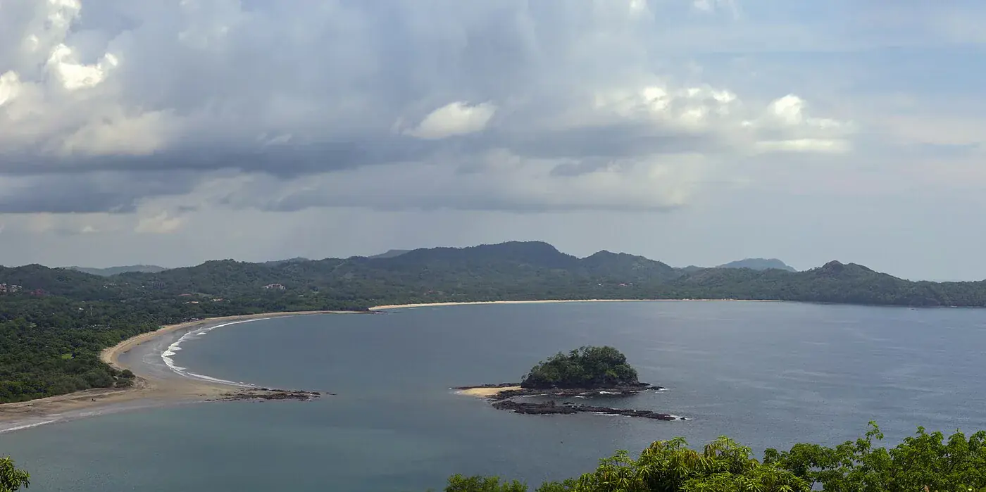 Elevated view north from Playa Flamingo over Brasilito Bay, with the pale curve of Playa Conchal, the wooded islet of Isla Loros in the bay and green headlands running into the distance