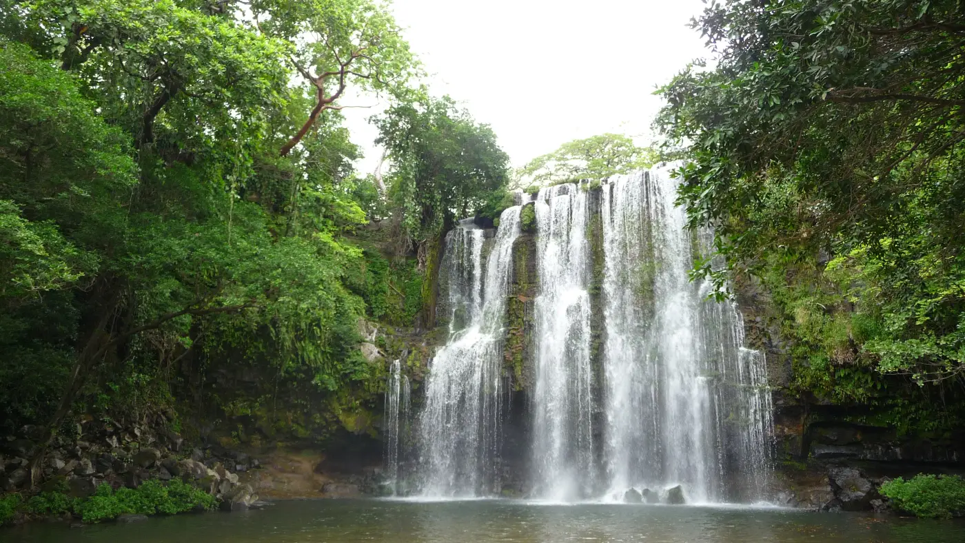 Llanos de Cortés waterfall near Bagaces, Guanacaste, falling in several white streams over a mossy rock wall into a pool, framed by trees