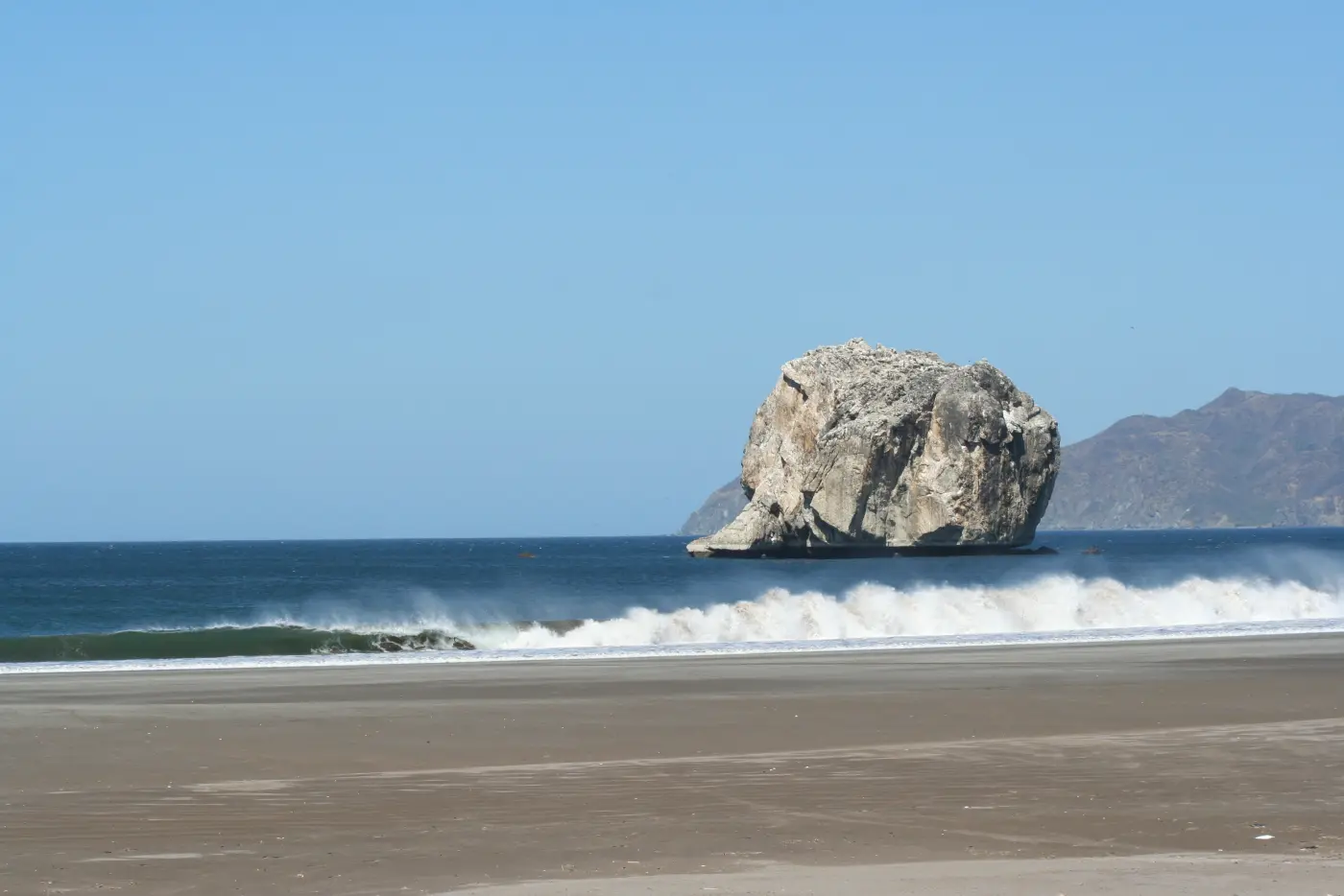 Witch’s Rock (Roca Bruja) rising offshore beyond breaking waves on the coast of Santa Rosa National Park, Guanacaste