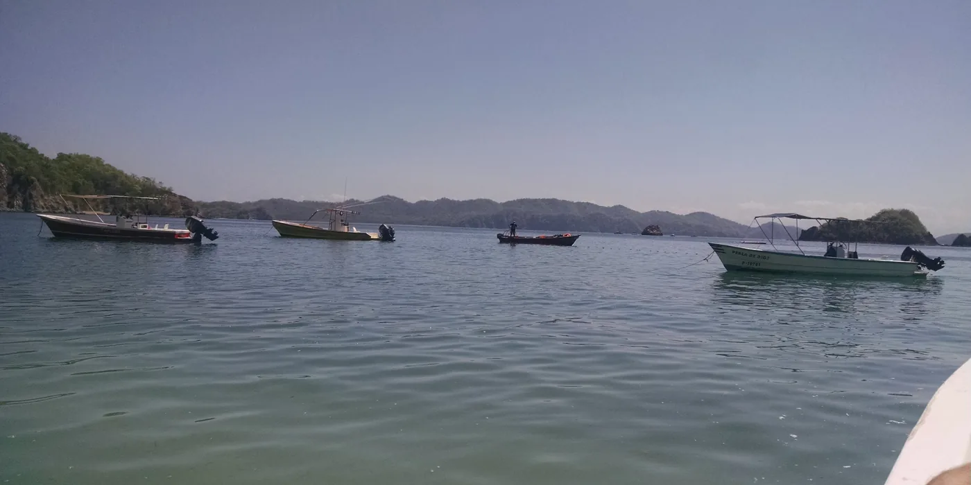 Tour boats anchored in turquoise shallow water off Isla Tortuga, with the island’s forested slope rising behind the beach