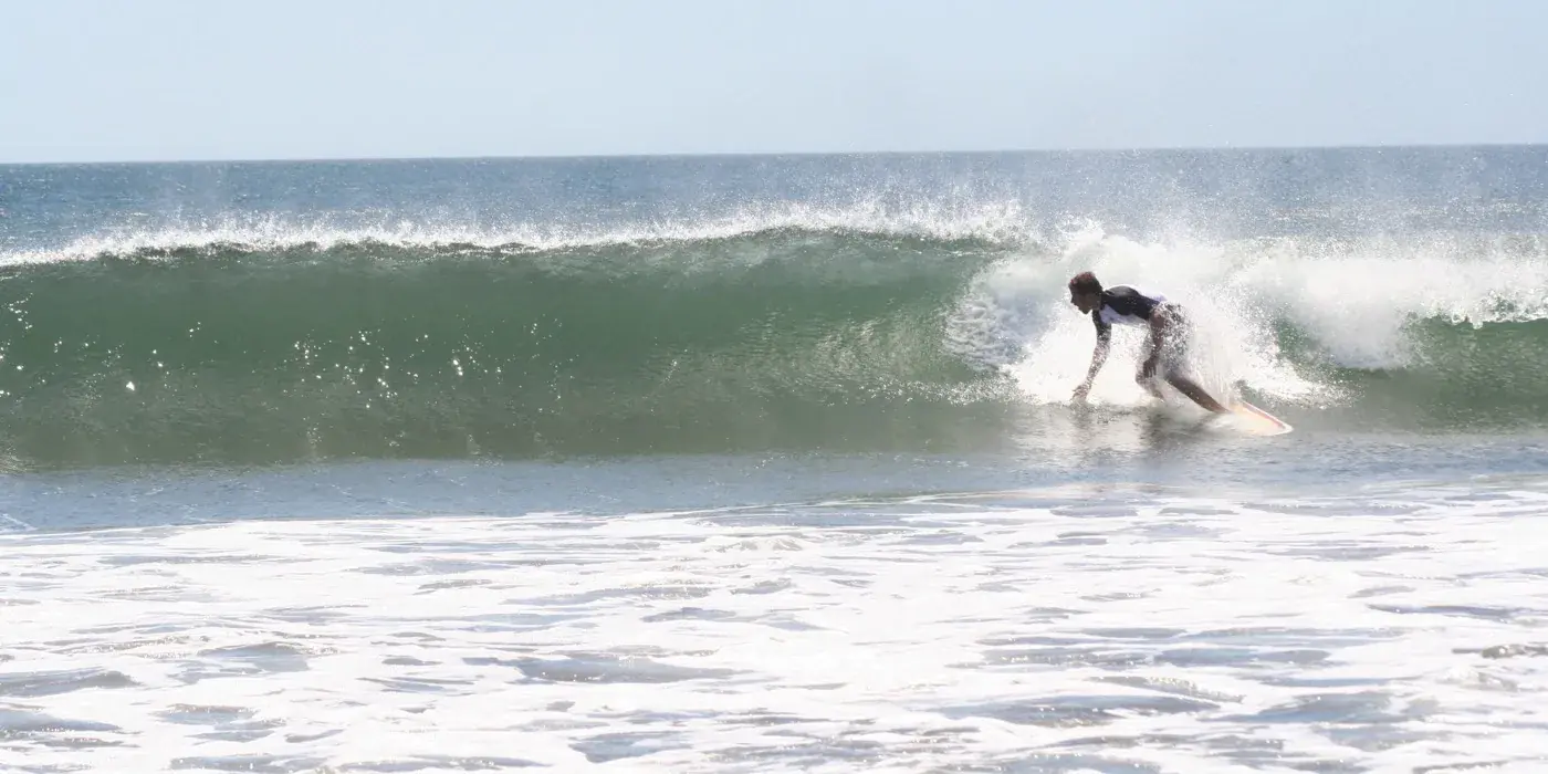 A surfer riding the face of a clean, chest-high breaking wave at Witch’s Rock on the Guanacaste coast, with white water spilling across the foreground