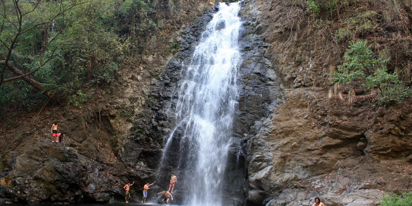 The Montezuma waterfall falling through a narrow forested gorge into a dark plunge pool surrounded by wet boulders