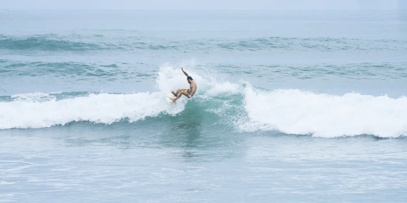 A surfer carving off the top of a chest-high wave at Playa Carmen on the Santa Teresa strip, with lines of whitewater behind and an overcast sky