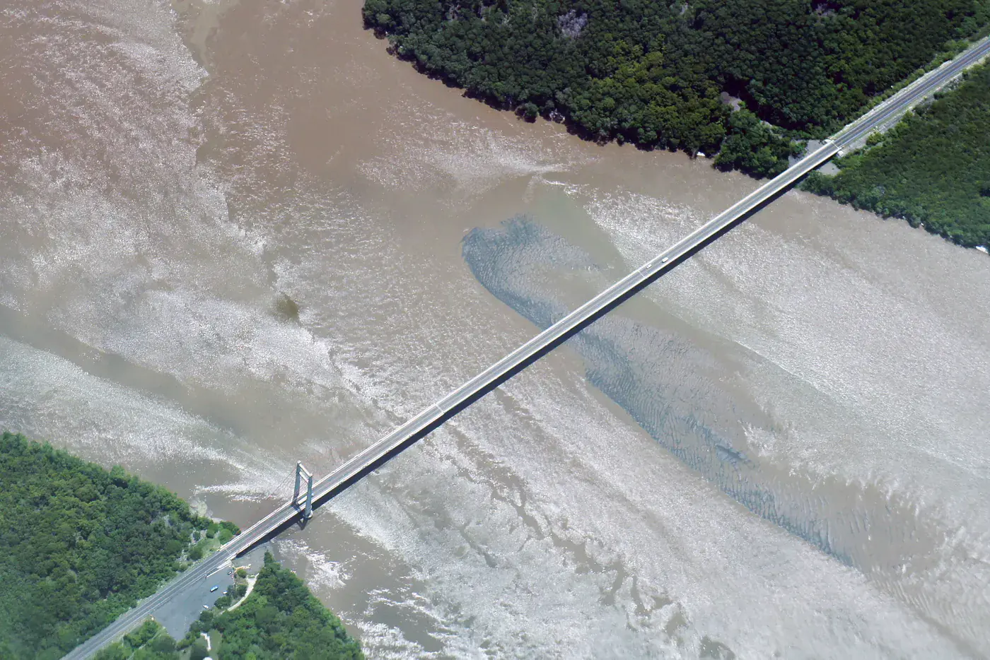 Aerial view of the Puente de la Amistad carrying a road diagonally across the wide, silt-patterned Río Tempisque into Guanacaste, Costa Rica, with a single vehicle crossing
