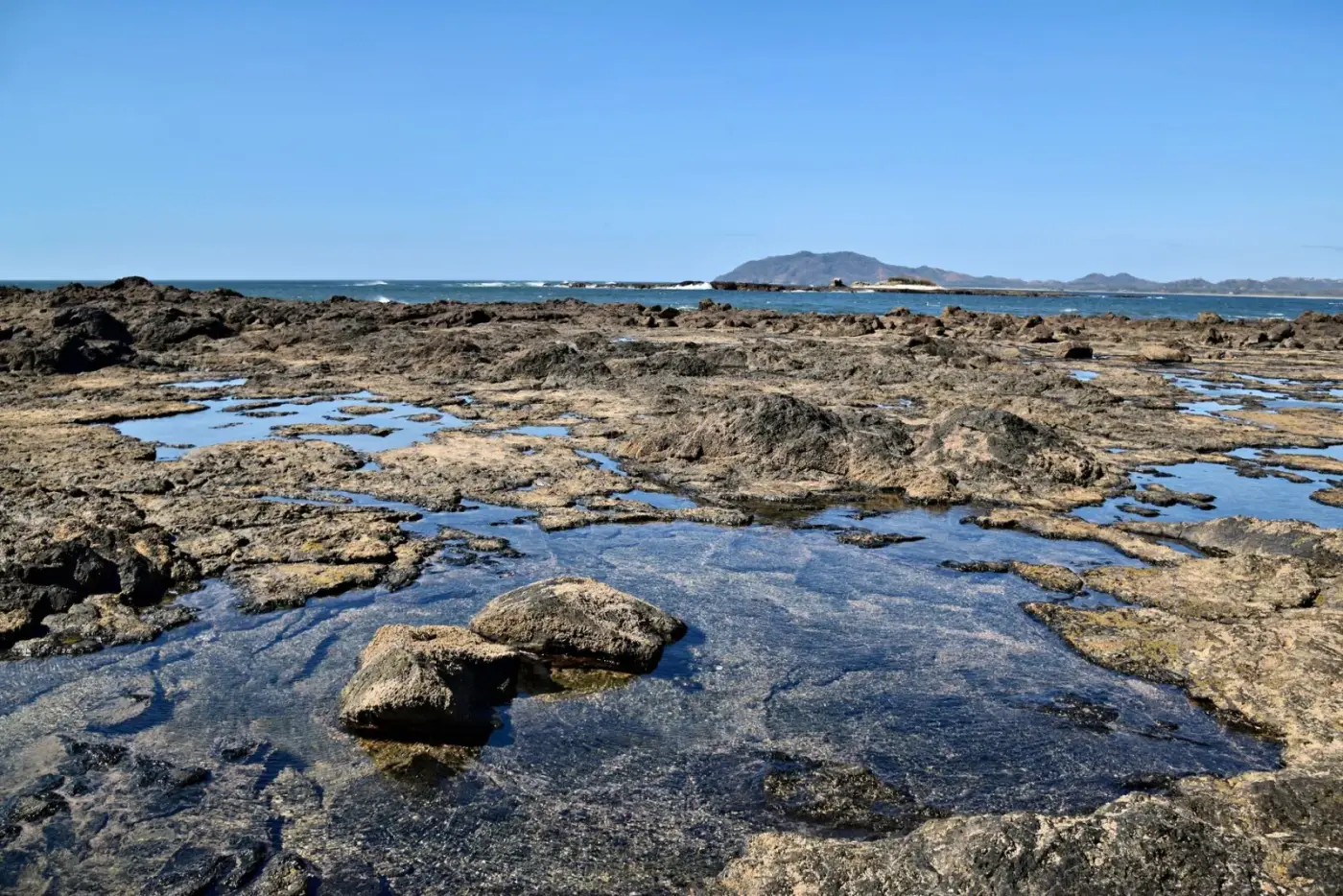 Explore the serene rocky coastline of Tamarindo Beach, Costa Rica under clear blue skies.