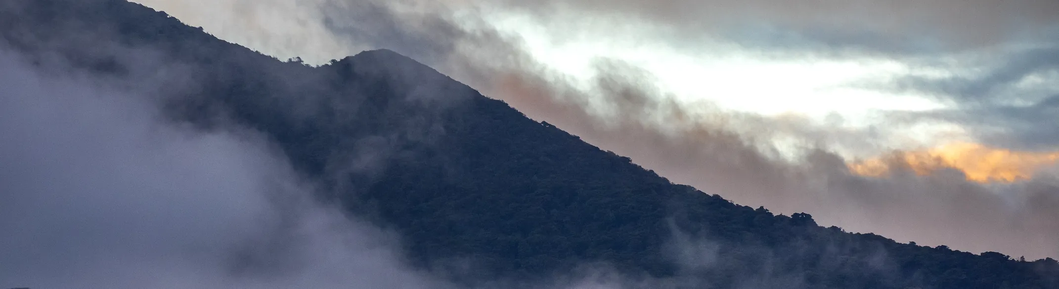 The forested ridge of Rincón de la Vieja at dusk, with cloud spilling over the slope
