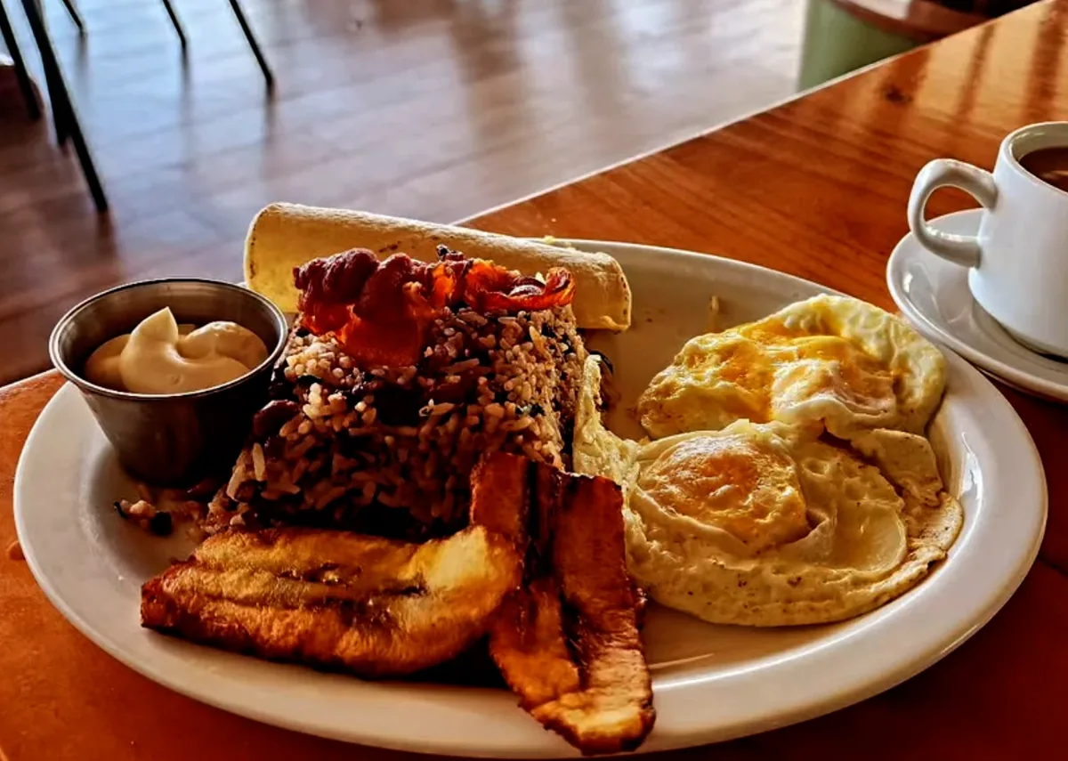 Costa Rican breakfast of gallo pinto with fried eggs, fried plantain, bacon, a flour tortilla and a cup of coffee