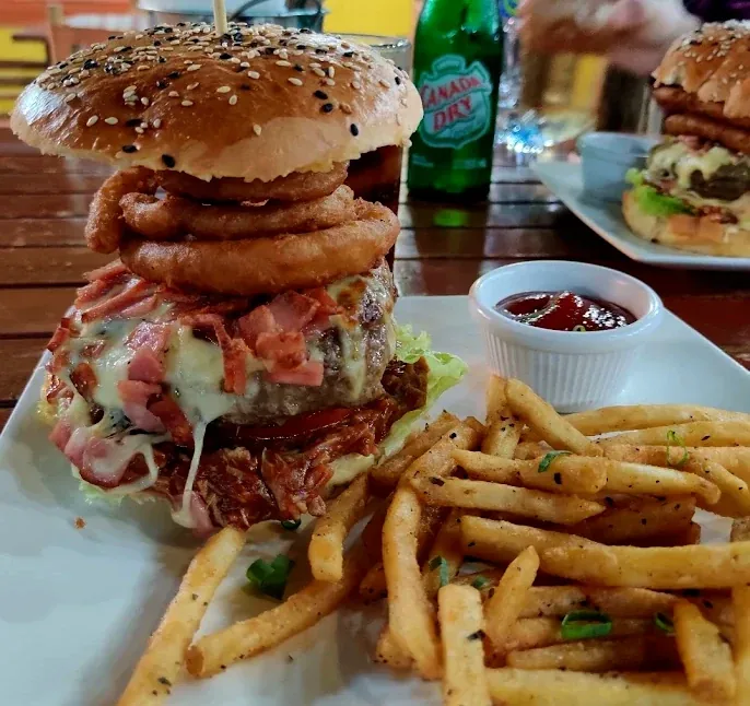 Stacked burger with onion rings, bacon and melted cheese in a sesame brioche bun, served with seasoned fries