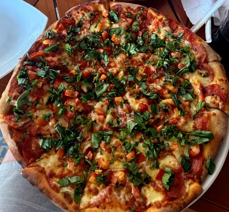 Whole pepperoni pizza scattered with fresh basil and chopped tomato