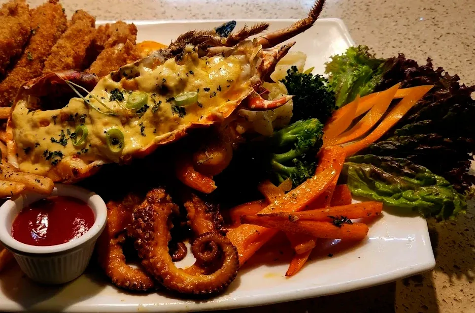 Seafood platter with half a grilled lobster under melted cheese, grilled octopus, breaded fish, broccoli and carrots