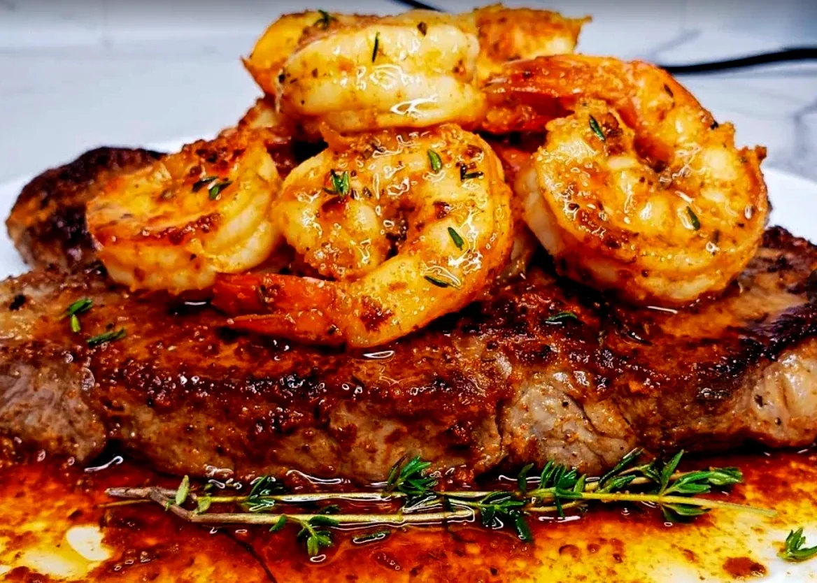 Grilled steak topped with garlic shrimp and fresh thyme, resting in its own juices